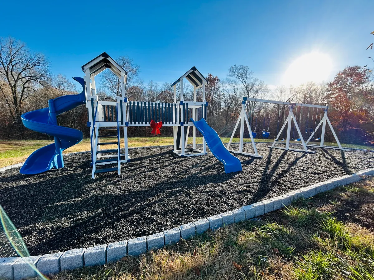 This image showcases a vibrant playground with blue slides and swings set in a cheerful outdoor environment. There are children playing and families gathered, suggesting an energetic and inviting space for playdates and family gatherings.