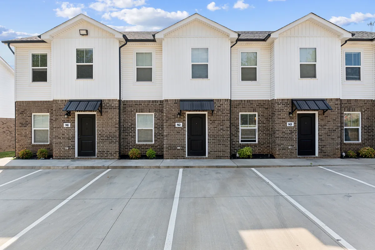An exterior view of the building's classic brick facade, black doors, and shuttered windows, suggesting a warm, welcoming entry point for guests and residents. The porch invites gatherings and downtime.