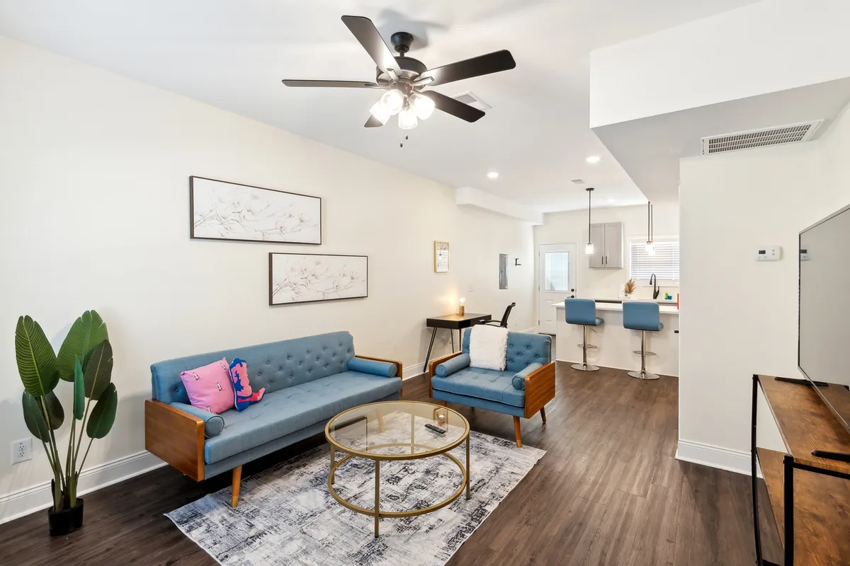 A bright, inviting living space featuring a comfortable sofa, stylish coffee table, modern artwork on the wall, and an open-concept kitchen area. The setting is designed for relaxation, socializing, or getting work done, making guests feel right at home.
