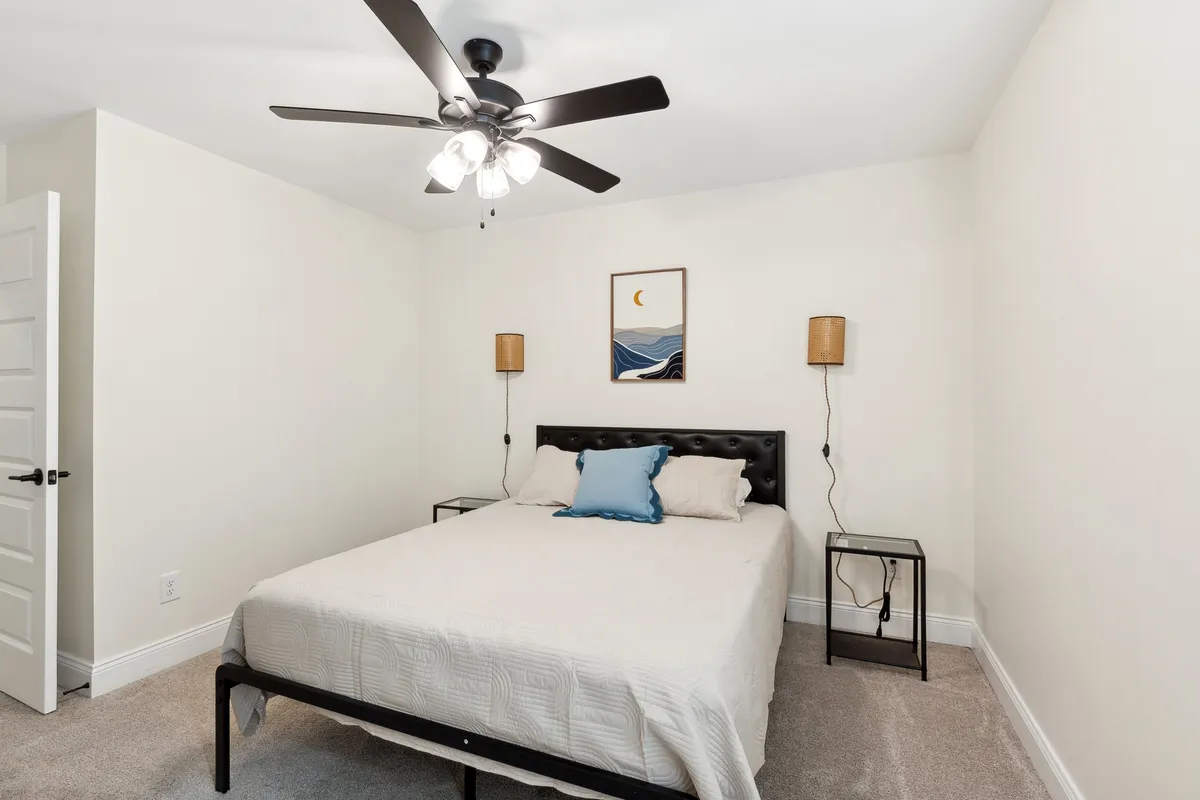 A serene bedroom scene with a cozy bed adorned with decorative pillows, gentle natural lighting from a nearby window, and calming wall art depicting waves and the moon. The overall ambiance is restful and welcoming, perfect for relaxing after a day out.