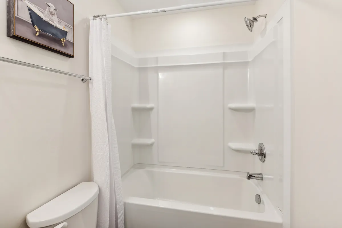 A calm, refreshing bathroom with a bathtub, showerhead, toilet, and tasteful artwork. The space is designed for both quick morning showers and relaxing evening baths, echoing a home-like, spa-inspired ambiance.