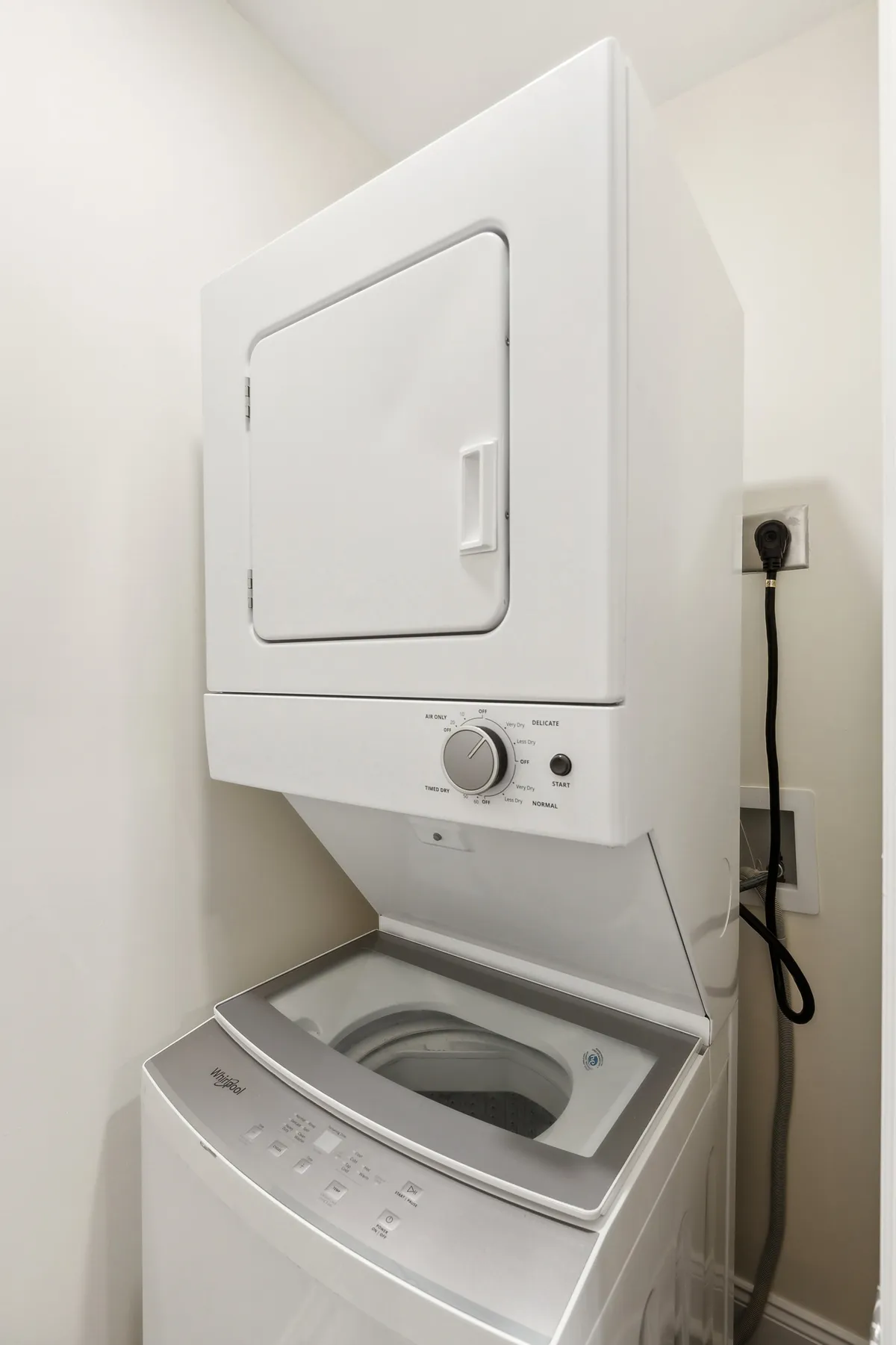 A compact laundry area showcases stacked washer and dryer units against clean white walls, creating a sense of order and efficiency. The design demonstrates practical storage for laundry essentials, further emphasizing convenience.