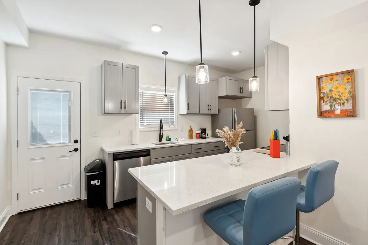 This image showcases a modern kitchen island with bar stools, decorative vase, and artwork on the wall, conveying a welcoming and functional kitchen space ideal for cooking, entertaining, and casual dining. The layout highlights both prep space and social gathering potential.
