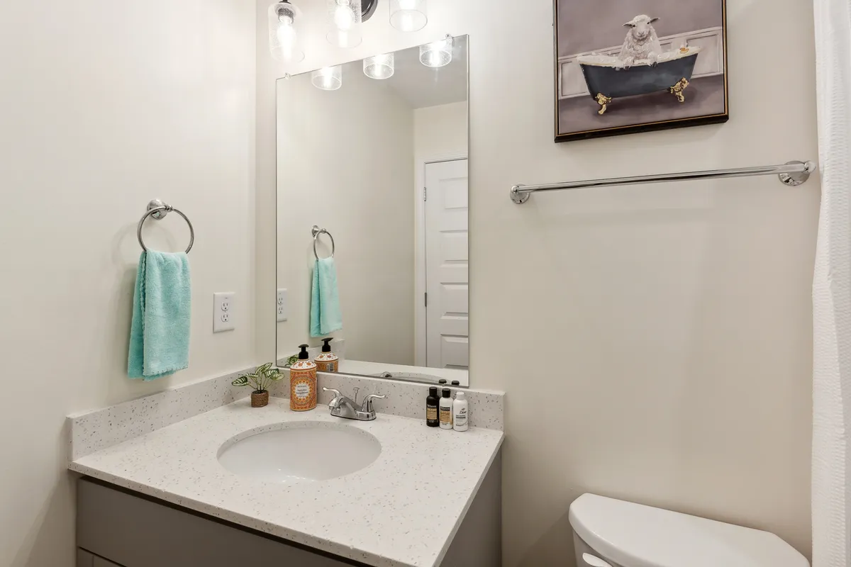 An inviting bathroom vanity area with a well-lit mirror, sink, plush towels, and decorative artwork. This space suggests moments of grooming, self-care, and peaceful morning rituals.